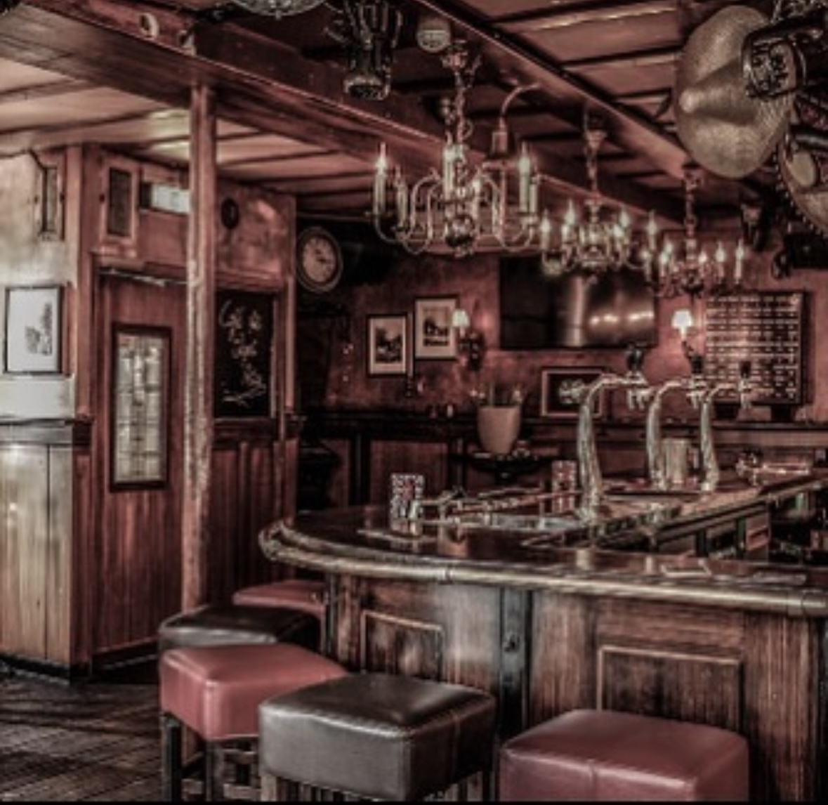De gebogen bar van Café de Engel met koperen biertaps, kroonluchters en rood leren krukken