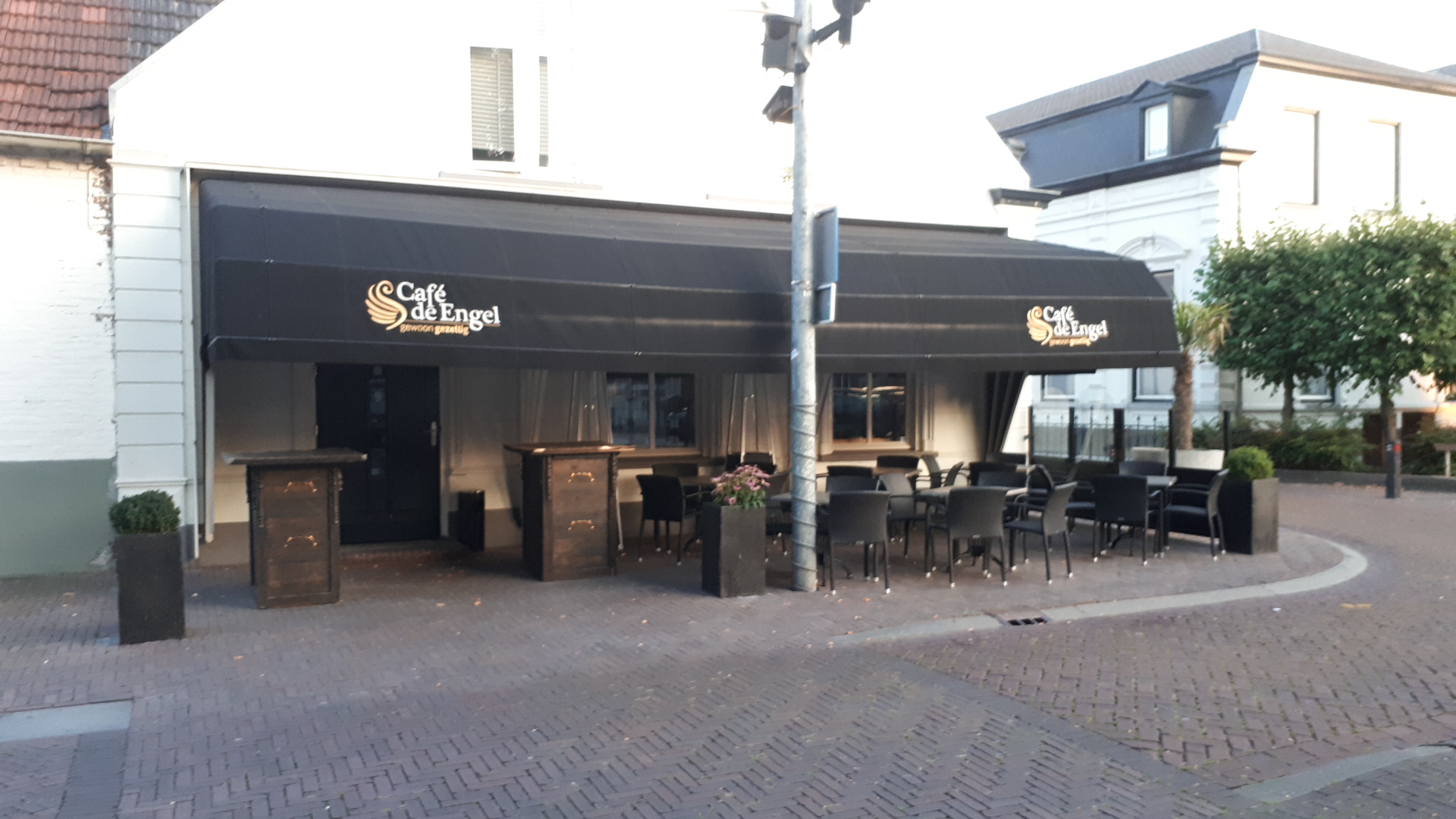 Het terras van Café de Engel met tafels en stoelen onder de zwarte luifel